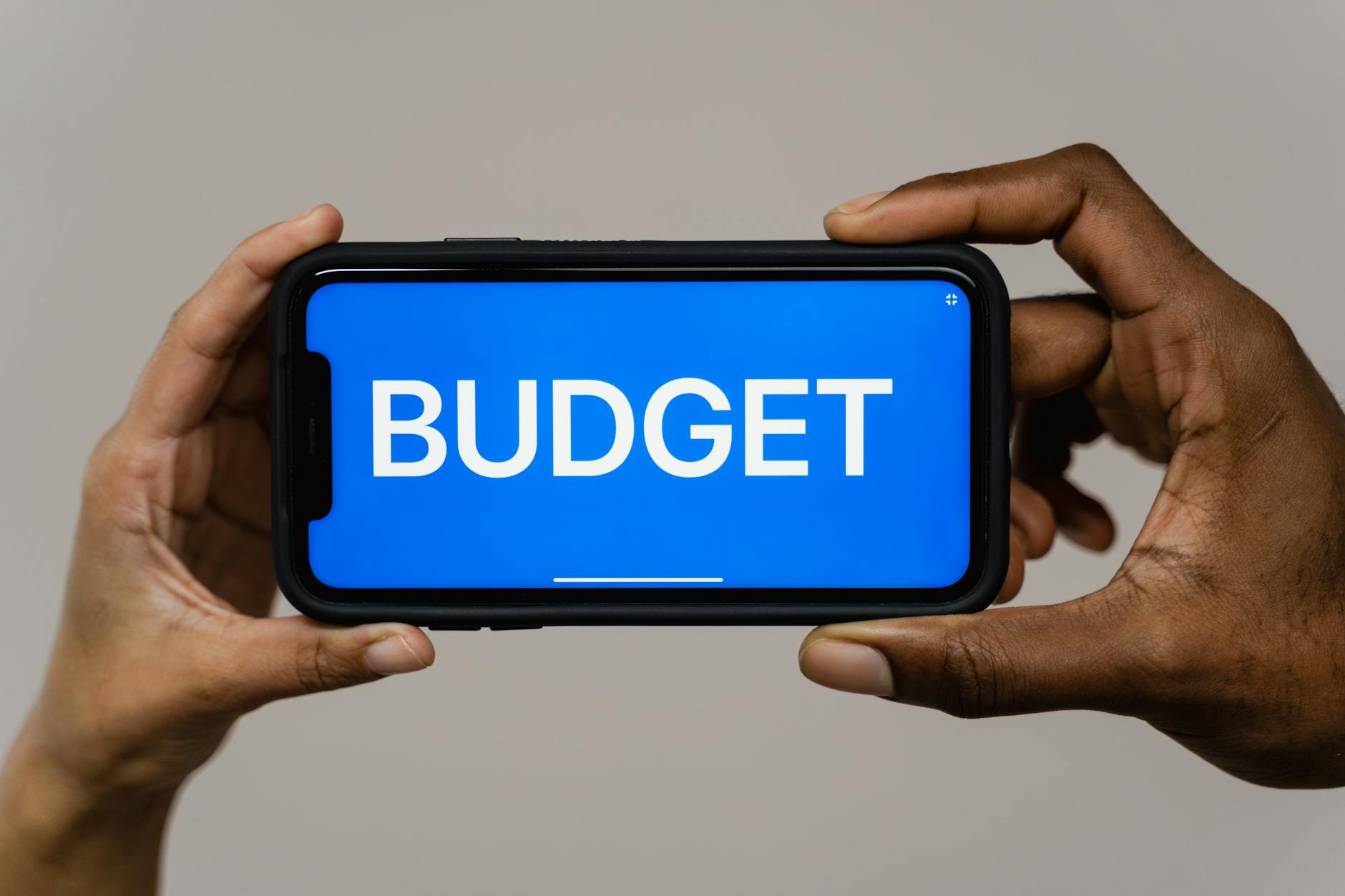 Two hands hold a smartphone displaying the word 'budget' on a blue screen, symbolizing financial planning.