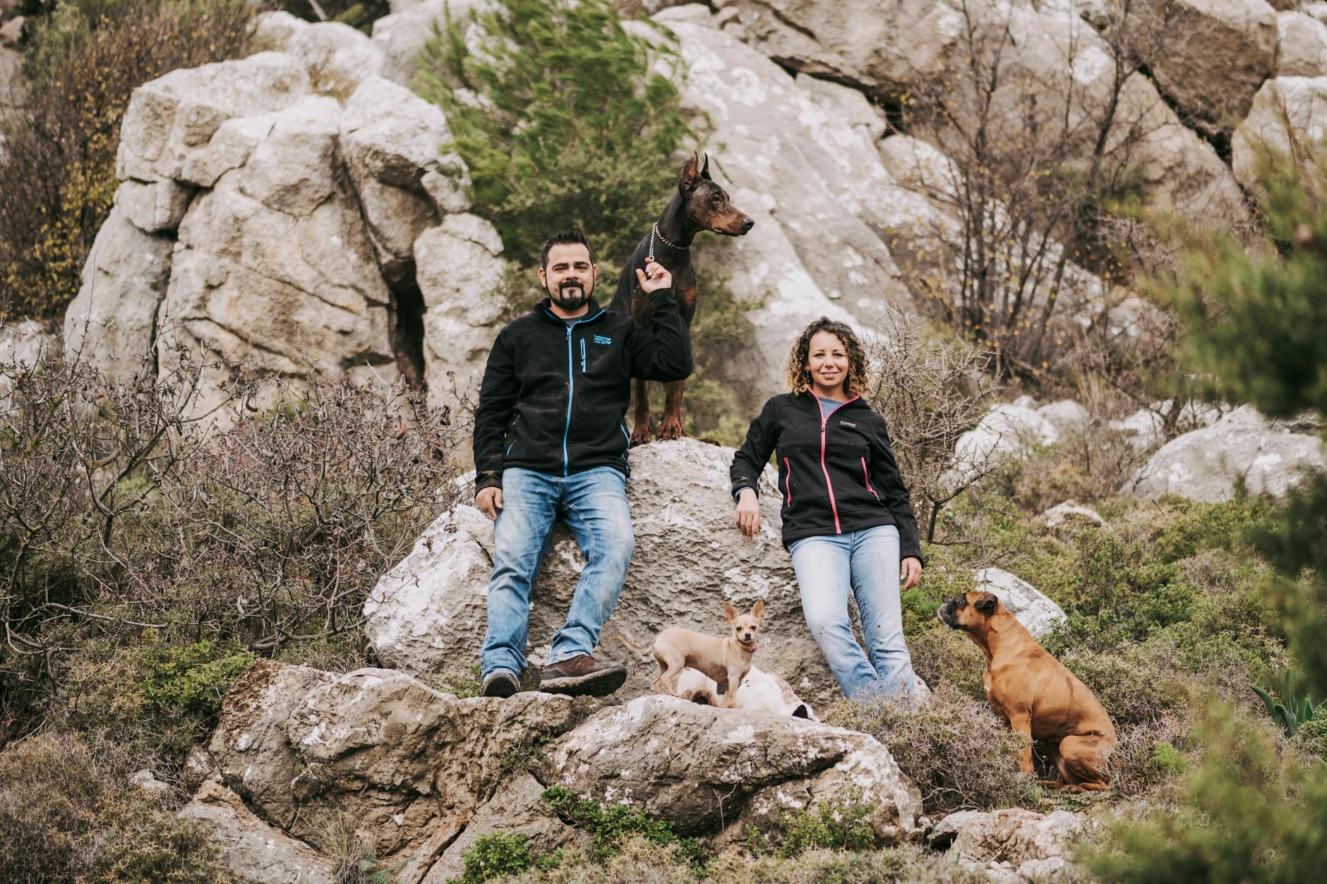 A couple enjoys hiking with their dogs on a scenic rocky terrain, showcasing adventure and companionship.