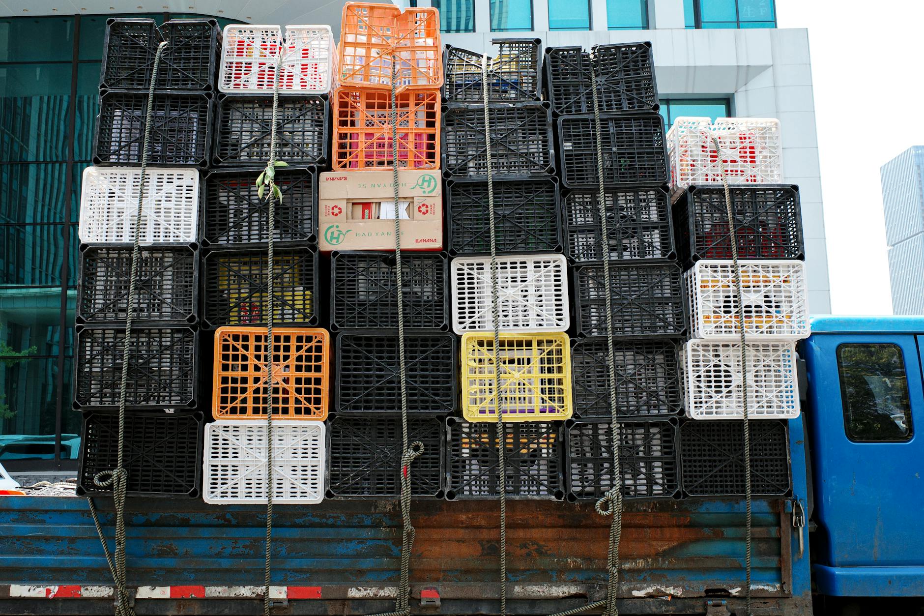Stacked colorful crates on a truck against a modern city building backdrop.