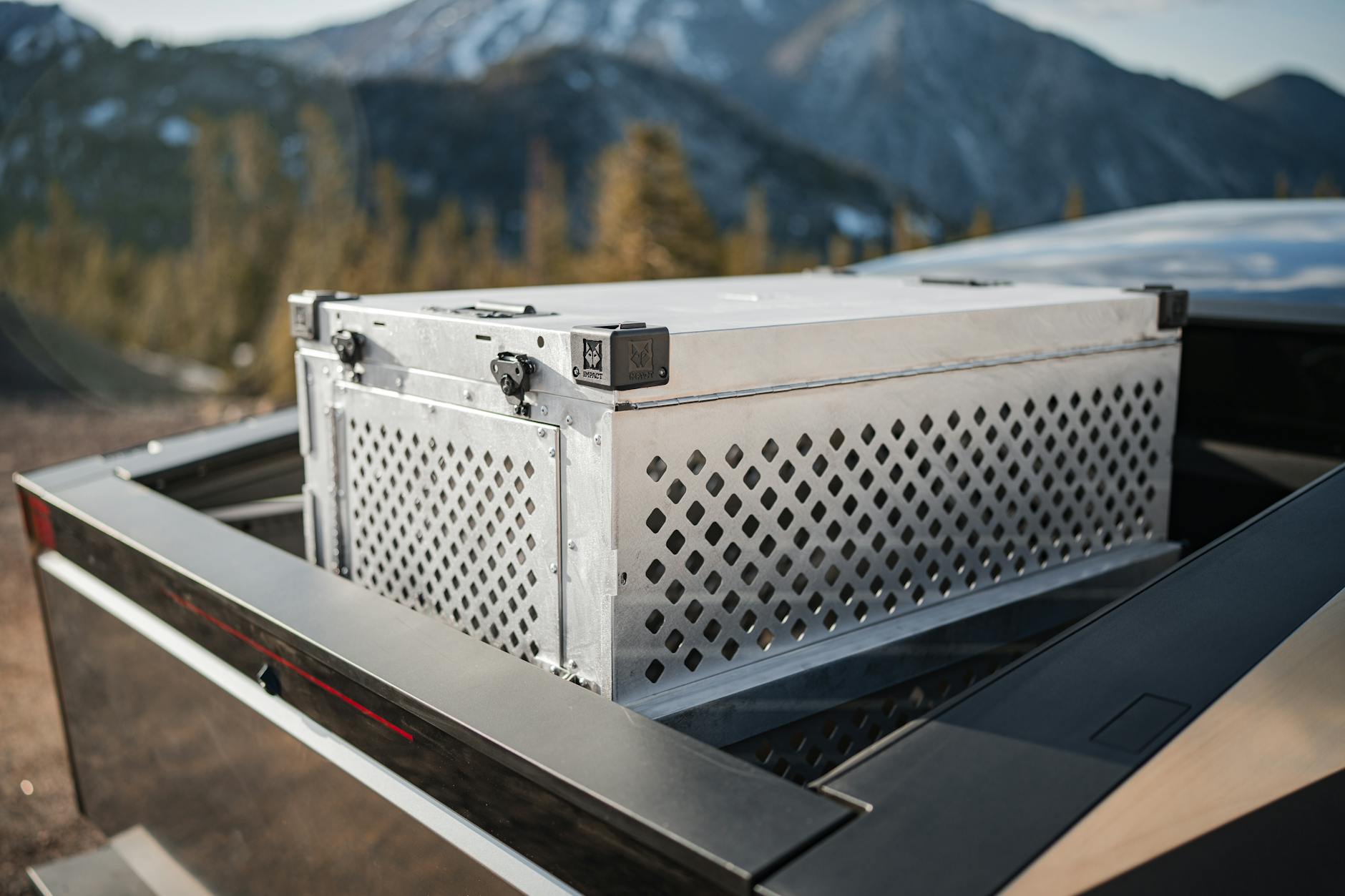 Secure metal dog crate mounted in a Tesla Cybertruck against a mountainous backdrop for outdoor adventures.