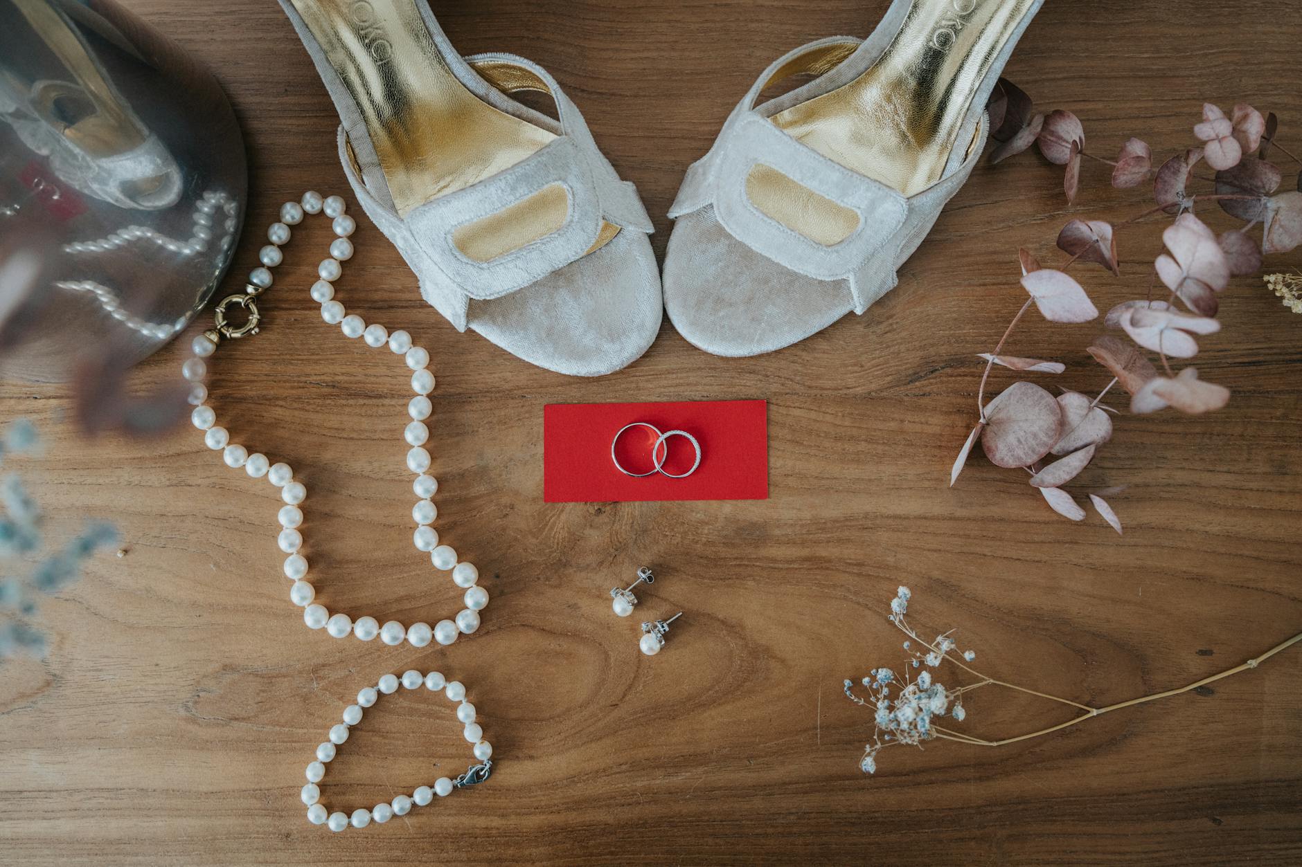 Top view of elegant wedding accessories including shoes, rings, and jewelry on wooden surface.