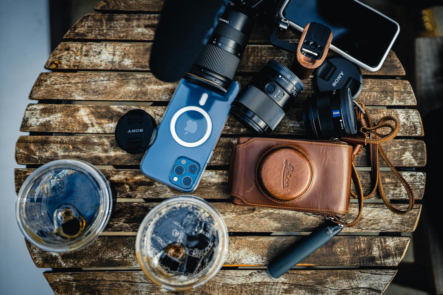 Top view of various photo cameras with lenses near modern cellphone and drinks placed on wooden table in light room