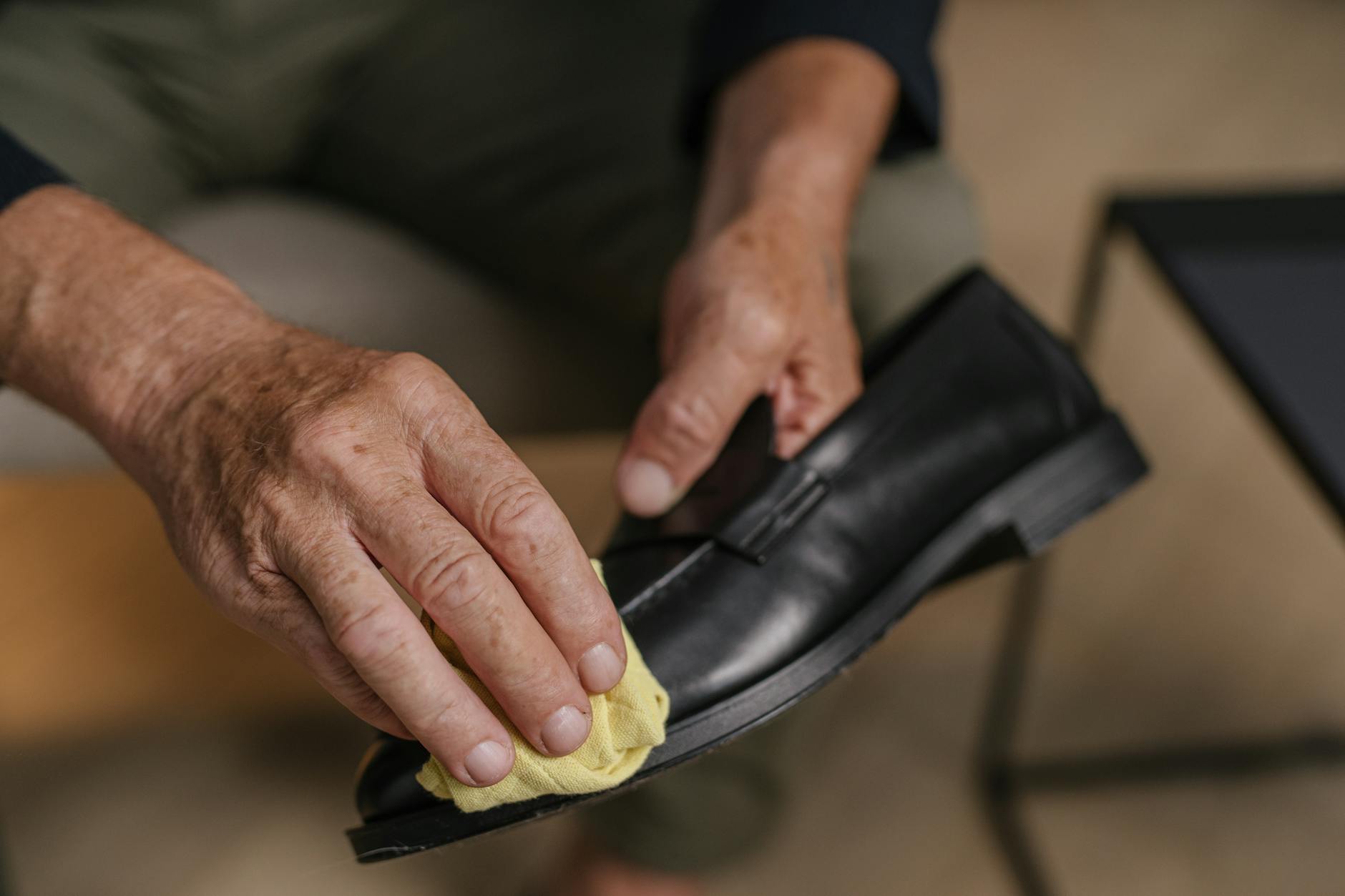 Detailed image of hands polishing a black leather shoe with a yellow cloth, emphasizing care and maintenance.