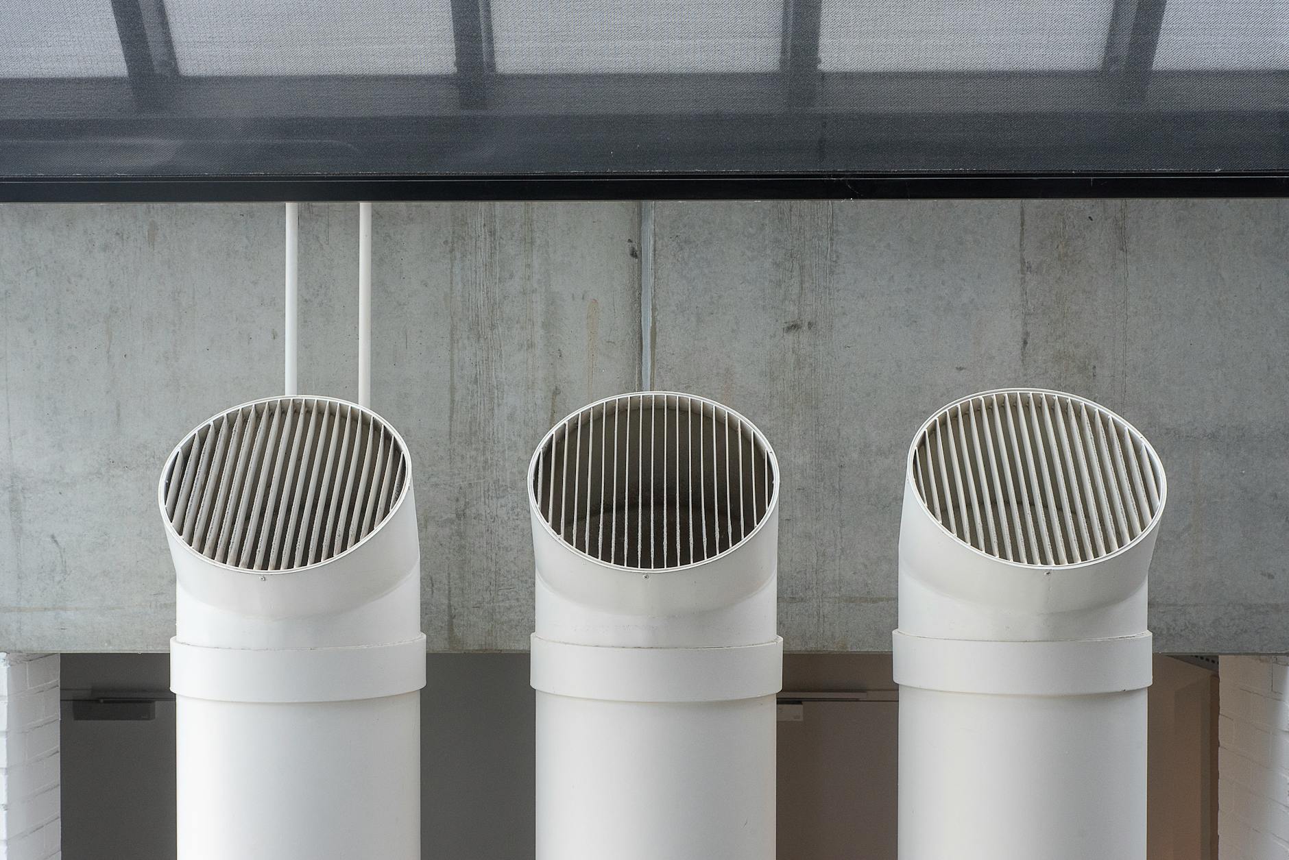 Three white industrial ventilation pipes aligned on concrete wall.