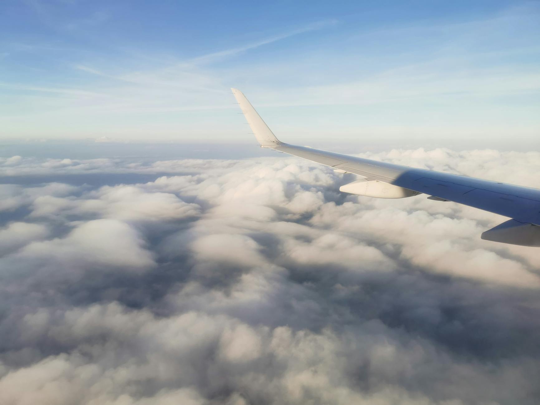 A serene view of an airplane wing flying above fluffy clouds on a clear day.